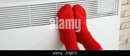 Frau in Stricksocken wärmt ihre Füße am Heizkörper zu Hause. Konzept der Heizperiode Stockfoto