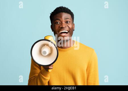 Fröhlicher schwarzer Kerl mit Megaphon, das Ankündigung macht Stockfoto