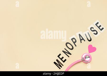 Wort-MENOPAUSE mit Stethoskop und Papierherz auf beigem Hintergrund Stockfoto