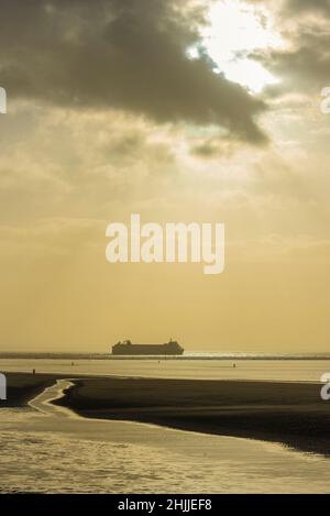 Crosby Strand am Fluss Mersey bei Sonnenuntergang an einem Winternachmittag mit einer Seatruck Ro Autofähre auf dem Weg zum Meer. Stockfoto