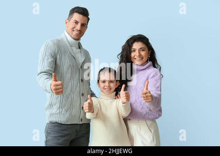 Das kleine Mädchen und ihre Eltern in warmen Pullovern, die auf hellem Hintergrund Daumen nach oben zeigen Stockfoto