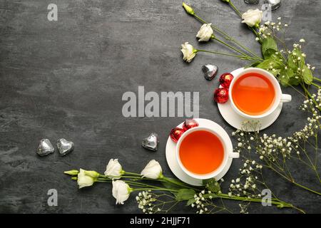 Leckere Schokoladen-Bonbons in Form von Herz, Blumen und Tassen mit Tee auf schwarzem Hintergrund. Valentinstag-Feier Stockfoto