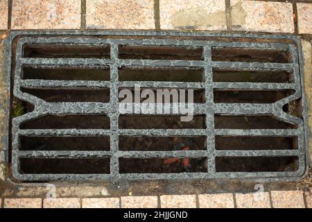 Sturmabfluss für die Wasserableitung. Details der städtischen Kommunikation. Luken des Kanals. Rost auf der Straße. Abfluss für Regenwasser. Stockfoto