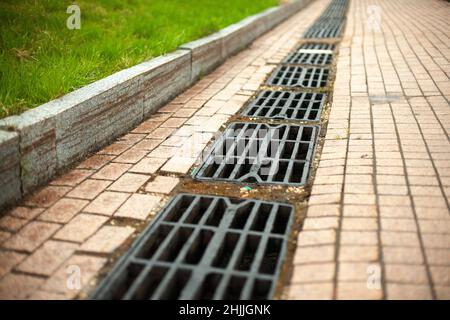 Sturmabfluss für die Wasserableitung. Details der städtischen Kommunikation. Luken des Kanals. Rost auf der Straße. Abfluss für Regenwasser. Stockfoto