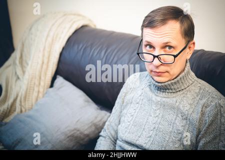 Schöner reifer Mann mit Brille, der sich zu Hause auf der Couch entspannt Stockfoto