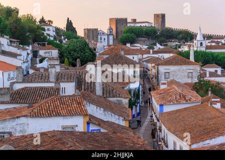 Landschaftlich schöne Aussicht auf weiße Häuser rot gefliesten Dächern. Und Burg von Obidos von der Mauer der Festung. Schöne Altstadt mit mittelalterlicher Architektur im Sonnenuntergang. Stockfoto