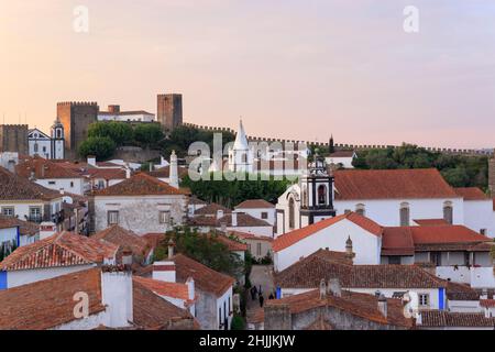 Landschaftlich schöne Aussicht auf weiße Häuser rot gefliesten Dächern. Und Burg von Obidos von der Mauer der Festung. Schöne Altstadt mit mittelalterlicher Architektur im Sonnenuntergang. Stockfoto