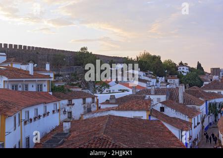 Landschaftlich schöne Aussicht auf weiße Häuser rot gefliesten Dächern. Und Burg von Obidos von der Mauer der Festung. Schöne Altstadt mit mittelalterlicher Architektur im Sonnenuntergang. Stockfoto