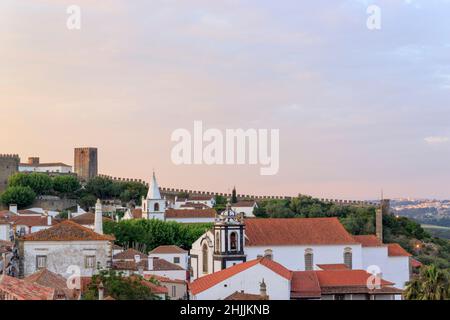 Landschaftlich schöne Aussicht auf weiße Häuser rot gefliesten Dächern. Und Burg von Obidos von der Mauer der Festung. Schöne Altstadt mit mittelalterlicher Architektur im Sonnenuntergang. Stockfoto