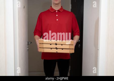 Pizzalieferer in roter Uniform, Boxen aus einer Pizzeria in den Händen eines Lieferers, Lieferservice Stockfoto
