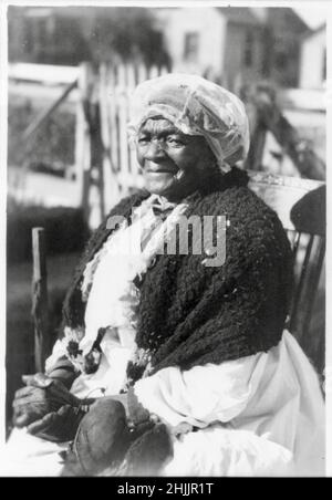 Mammy Prater trägt einen schweren Schal und eine Mütze, die draußen in einem Schaukelstuhl sitzt und die Hände in den Schoß geklammt sind - ehemaliger Sklave, der zum Zeitpunkt der Fotografie 115 Jahre alt war. Stockfoto