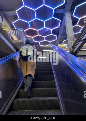 Sie fahren die Rolltreppe hinauf, die den U-Bahnsteig Broadway/Lafayette F mit dem Zug Bleeker Street Uptown 6 in Manhattan mit seiner Neonkunstdecke verbindet. Manhattan, NYC. Stockfoto