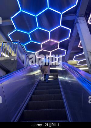 Sie fahren die Rolltreppe hinauf, die den U-Bahnsteig Broadway/Lafayette F mit dem Zug Bleeker Street Uptown 6 in Manhattan mit seiner Neonkunstdecke verbindet. Manhattan, NYC. Stockfoto