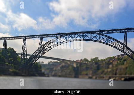 Tilt-Shift-Effekt-Fotografie. Maria-Pia-Brücke über den Douro-Fluss, Porto, Portugal. Panoramablick vom Wasser. Schmiedeeiserne Eisenbahnbrücke. Eins Stockfoto