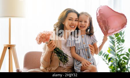 Guten Tag! Die Tochter gratuliert der Mutter und schenkt ihr Blumen. Mama und Mädchen lächeln und umarmen. Familienurlaub und Zweisamkeit. Stockfoto