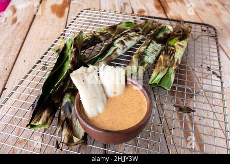 Gegrillter Fischkuchen aus gemahlenem Makrelenfisch, gemischt mit Gewürzen, dann in Bananenblätter gewickelt, über Holzkohle gegrillt, mit Erdnusssoße gegessen Stockfoto