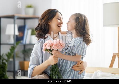 Guten Tag! Die Tochter gratuliert der Mutter und schenkt ihr Blumen. Mama und Mädchen lächeln und umarmen. Familienurlaub und Zweisamkeit. Stockfoto