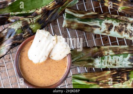 Gegrillter Fischkuchen aus gemahlenem Makrelenfisch, gemischt mit Gewürzen, dann in Bananenblätter gewickelt, über Holzkohle gegrillt, mit Erdnusssoße gegessen Stockfoto