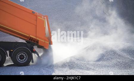 Kipper schüttet Haufen Schutt aus. Archivmaterial. Muldenkipper auf der Baustelle schüttet Schutt auf dem Hintergrund eines Gesteinsstapels aus. Stockfoto