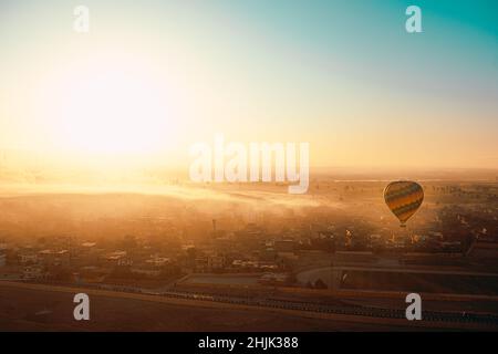 Sehr helle Szene eines frühen Morgenaufgangs in luxor ägypten, ein einziger Heißluftballon steigt über die Landschaft. Nebliger Morgen über dem ägyptischen la Stockfoto