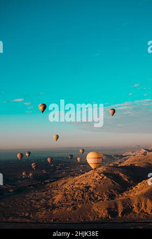 Atemberaubende vertikale Aufnahme von Dutzenden Heißluftballons, die um das luxor-gebiet in ägypten fliegen. Wüstenorangenbereich am frühen Morgen. Strahlend blauer Himmel Stockfoto
