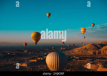 Weite Sicht auf Dutzende von Heißluftballons, die um die gegend von luxor in ägypten fliegen. Beliebte touristische Aktivität, herrliche Aussicht auf die umliegende Wüste Stockfoto