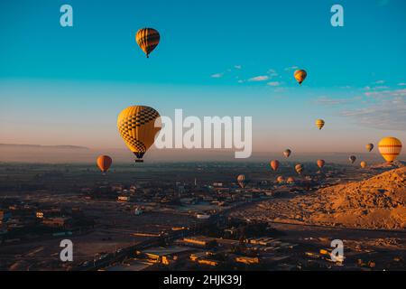 Weite Sicht auf Dutzende von Heißluftballons, die um die gegend von luxor in ägypten fliegen. Beliebte touristische Aktivität, herrliche Aussicht auf die umliegende Wüste Stockfoto