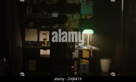 Müder junger Mann, der abends zu Hause mit einem Laptop arbeitet. Lager. Trauriger einsamer Mann, der zu Hause am Tisch sitzt. Das Konzept der Einsamkeit. Stockfoto