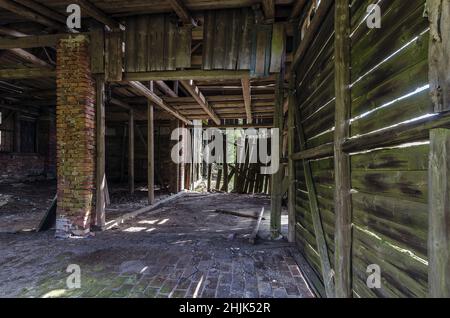 Alte verlassene rustikale Scheune mit undichten Holzwänden und kaputtem Tor Stockfoto