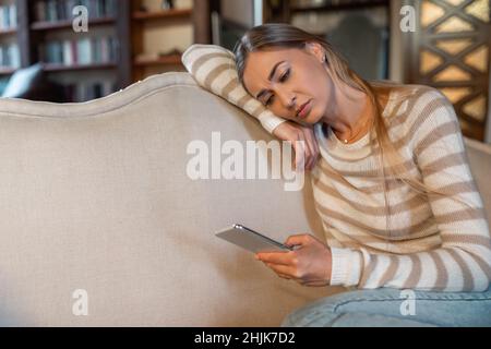 Traurige Dame, die Handy benutzt und auf den Bildschirm schaut Stockfoto