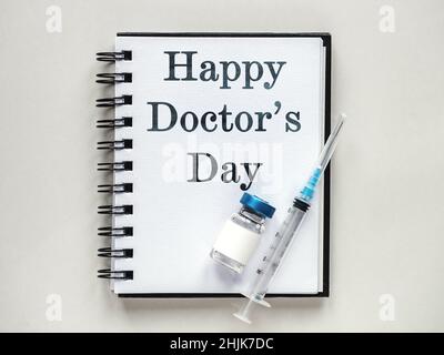 Alles gute zum Tag des Arztes. Spritzen, Injektionsfläschchen und ein Notizblock liegen auf dem Tisch. Nahaufnahme, drinnen, Ansicht von oben. Tageslicht, Studiofoto. Healthcar Stockfoto