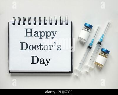 Alles gute zum Tag des Arztes. Spritzen, Injektionsfläschchen und ein Notizblock liegen auf dem Tisch. Nahaufnahme, drinnen, Ansicht von oben. Tageslicht, Studiofoto. Healthcar Stockfoto