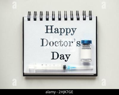 Alles gute zum Tag des Arztes. Spritzen, Injektionsfläschchen und ein Notizblock liegen auf dem Tisch. Nahaufnahme, drinnen, Ansicht von oben. Tageslicht, Studiofoto. Healthcar Stockfoto