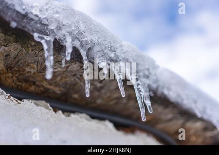 Kleine Eiszapfen hängen vom Holzdach. Stockfoto