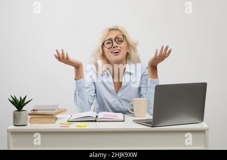 Überfordert frustrierte Geschäftsfrau, die langweilige Arbeit verrichten und auf hellgrauem Hintergrund am Arbeitsplatz sitzen Stockfoto