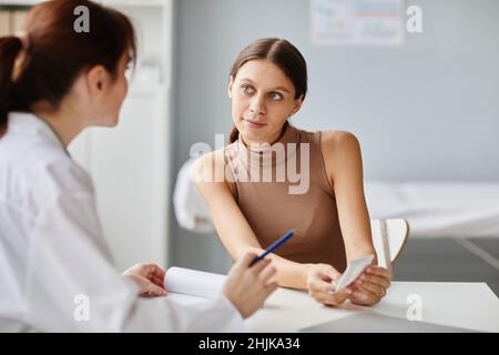 Junge Frau zeigt dem Arzt das Ultraschallbild ihres Babys und diskutiert es, während sie am Tisch im Arztbüro sitzt Stockfoto