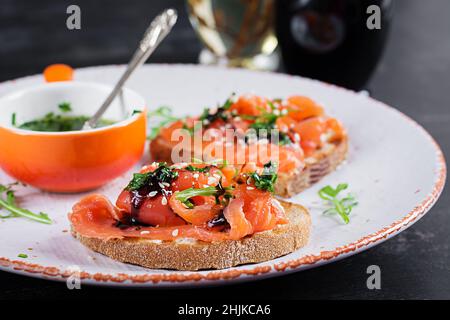 Gesundes Toast mit Lachs, Frischkäse, Sesam, schwarzem Pfeffer und Rucola auf dem Teller. Stockfoto