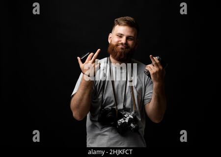 Professioneller hübscher bärtiger männlicher Fotograf mit einer Reihe von Vintage-Fotokameras zeigt einen Mittelfinger mit beiden Händen im Fotostudio. Stockfoto