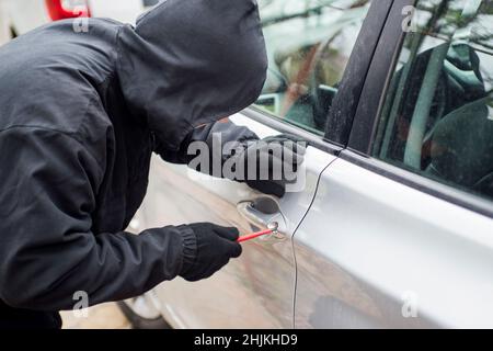 Räuber Mann in schwarzer Kapuzenjacke mit einem Schraubendreher zu brechen Schloss und ein Fahrzeug zu stehlen. Autodieb oder Diebstahl für Versicherungskonzept. Stockfoto