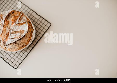 Ein Laib hausgemachtes Sauerteigbrot mit Mohnsamen auf einem Kühlregal auf beigem Hintergrund. Der Hintergrund ist unscharf. Stockfoto