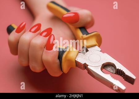 Nahaufnahme einer weiblichen Hand mit roter Maniküre und Zange. Stockfoto