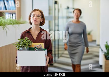 Waist-up-Porträt einer jungen Frau, die Box mit persönlichen Gegenständen bei einem neuen Job trägt, Platz kopieren Stockfoto