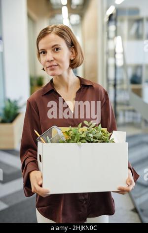 Vertikale Taille bis Porträt einer jungen Frau mit Box mit persönlichen Sachen beim Start neuer Job Stockfoto