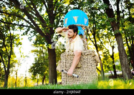 Ein großer erwachsener bärtiger Mann im Korb eines Spielzeugballons. Stockfoto