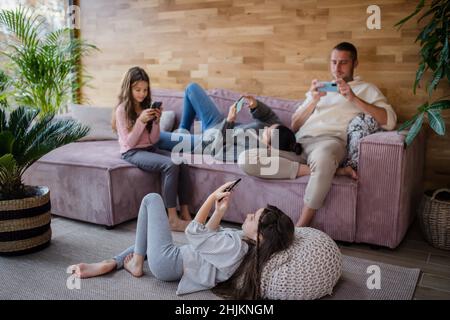 Familie mit zwei kleinen Töchtern, jeder nutzt Handy im Wohnzimmer. Stockfoto