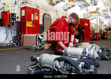 PHILIPPINISCHES MEER (Jan 22, 2022) Schaden Controlman Fireman Luke Thorpe aus Lancaster, Kalifornien, füllt Flaschen mit autarem Atemgerät (SCBA) in der Hangarbucht an Bord des Flugzeugträgers USS Abraham Lincoln (CVN 72) der Nimitz-Klasse auf. Abraham Lincoln, der als Teil der US-Pazifikflotte tätig ist, führt Schulungen durch, um eine freie und offene Region im Indo-Pazifik-Raum zu erhalten und zu schützen. Stockfoto