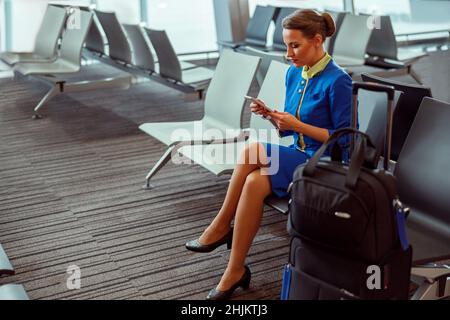 Weibliche Flugbegleiterin, die im Flughafenterminal ein Mobiltelefon benutzt Stockfoto