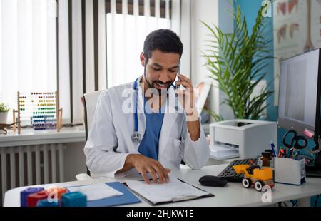 Junger männlicher Arzt, der Telefonanrufe in seinem Büro managt. Stockfoto