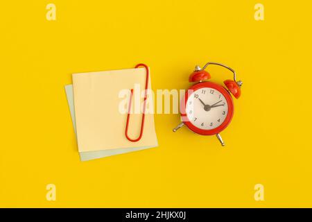 Roter Wecker und Haftnotizen mit Platz für Text auf gelbem Hintergrund Stockfoto