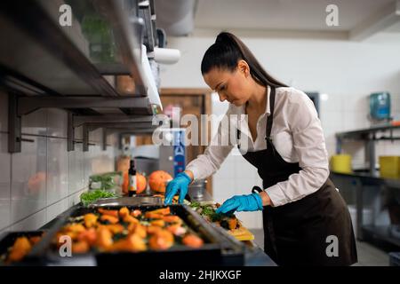 Professionelle Köchin, die in der Restaurantküche an ihren Gerichten arbeitet. Stockfoto